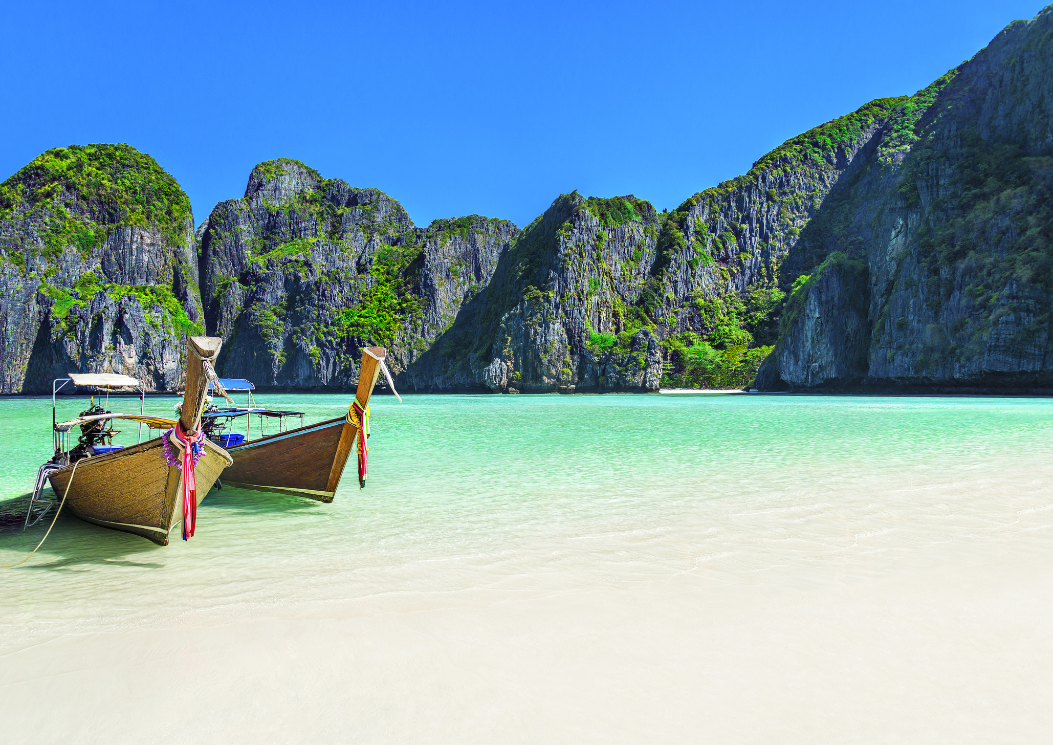 Famous scenic Maya Bay beach at Ko Phi Phi Leh Island with two traditional longtail taxi boats mooring and steep limestone hills in background, Thailand, part of Krabi Province, Andaman Sea